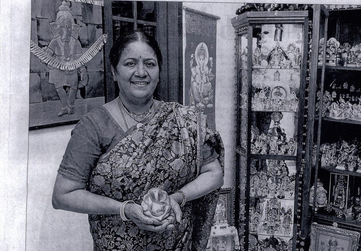 Banooravi at home in Singapore, holding a small Pillaiyar figure, with part of her collection displayed in wooden cabinets. Tamil Murasu, September 2012.